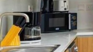 A compact kitchen with wooden cabinets, a microwave, a coffee maker, and a sink. - -Bloomfields Modern 1BR in Oasis Masd (Abu Dhabi)