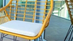 A yellow wicker chair with a white cushion on a balcony with glass doors. - -Bloomfields Modern 1BR in Oasis Masd (Abu Dhabi)