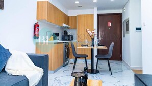 A modern kitchen with wooden cabinets, a dining table with chairs, a coffee machine, and a fire extinguisher. - -Bloomfields Modern 1BR in Oasis Masd (Abu Dhabi)