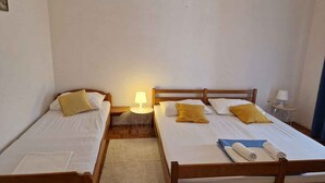 Una habitación con dos camas de madera, cada una con ropa blanca y almohadas amarillas. Hay una pequeña mesa redonda con una lámpara entre las camas.