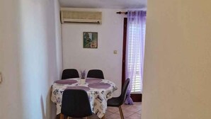 Un pequeño comedor con una mesa, sillas, un equipo de aire acondicionado y una ventana con cortinas.