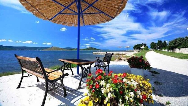 Un patio frente al mar con una mesa, sillas, un paraguas y un arreglo floral.