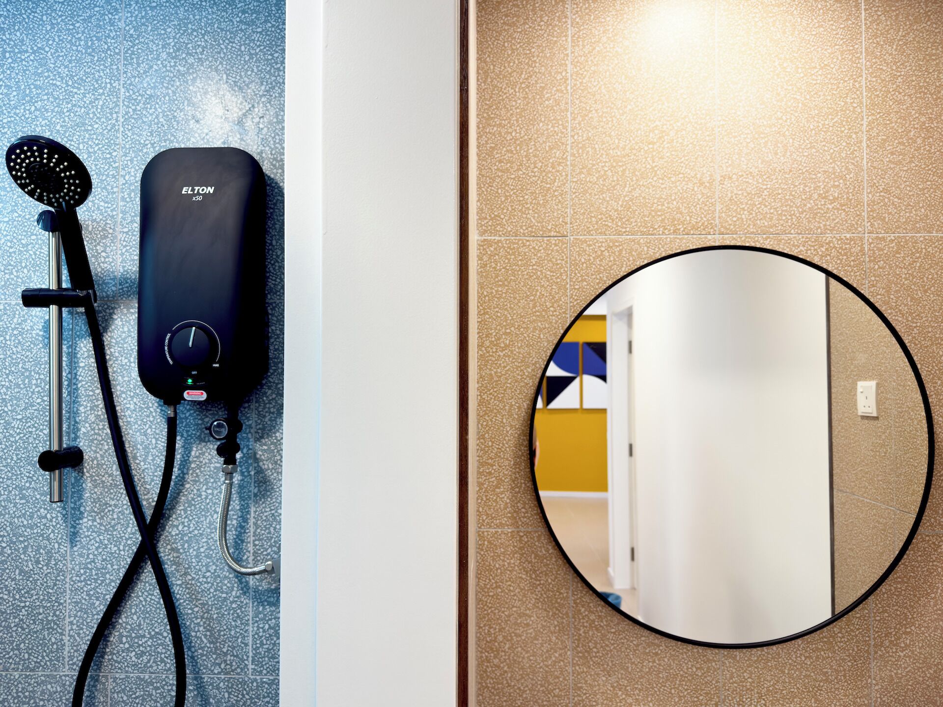 Un baño con ducha, un calentador de agua negro y un espejo redondo en la pared.
