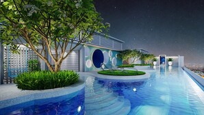 Une piscine à débordement moderne offrant une vue sur le ciel nocturne, entourée d’une végétation luxuriante et d’un bâtiment contemporain doté de fenêtres rondes.
