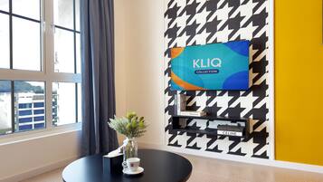 A modern room with a large window, a round black table with a vase and a cup, a houndstooth patterned wall, and a mounted TV displaying 'KLIQ COLLECTION'.