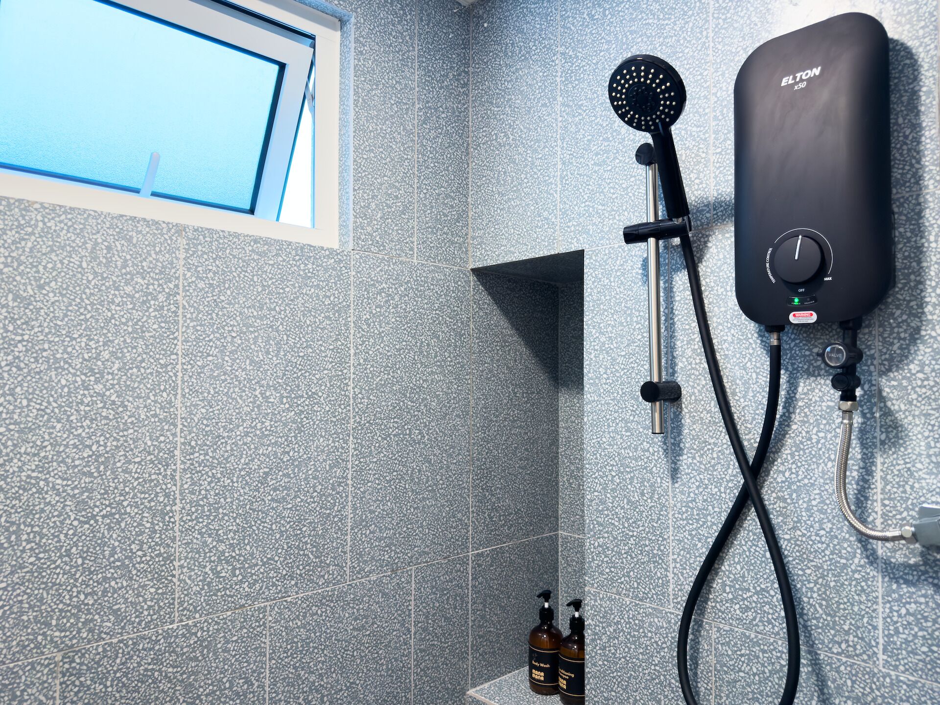 Un espace douche équipé d’un pommeau de douche à main, d’un panneau de commande mural et de deux bouteilles de shampoing.