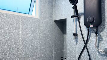 A shower area with a handheld showerhead, a wall-mounted control unit, and two bottles of shampoo.