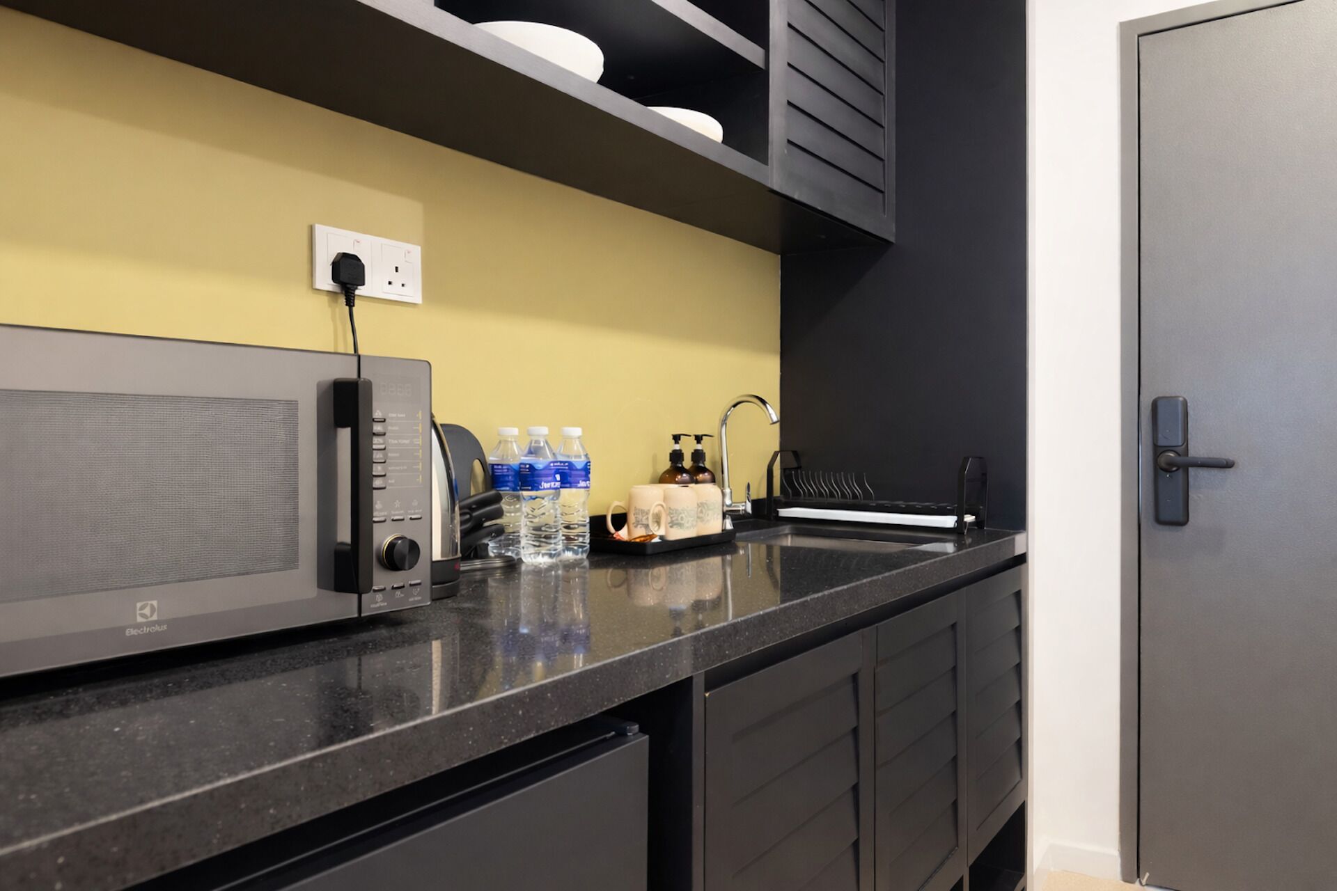Uma cozinha moderna com bancada preta, micro-ondas e dispensador de água.