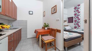 Quarto compacto com cozinha compacta, área de refeições com mesa e cadeiras, e uma cama com cortina estampada.