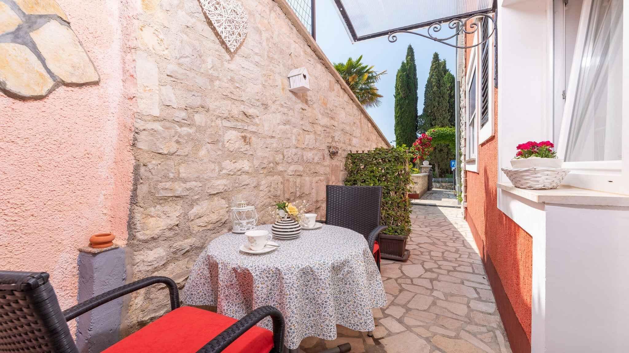 Un pequeño espacio al aire libre con una mesa y sillas, un muro de piedra y un estrecho sendero que lleva a una puerta.