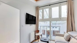 Una sala de estar moderna con un ventanal grande, un televisor de pantalla plana, un sofá, un sillón y una mesita.