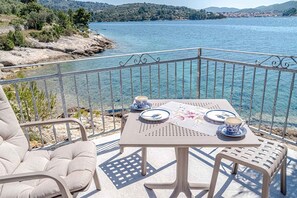 A balcony with a table set for two, overlooking a body of water and a hilly landscape. - Holiday home mit Terrasse und Meerblick (Vela Luka)