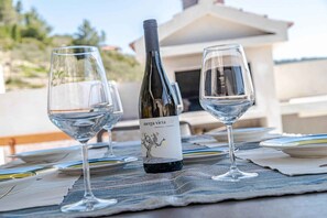 A table set with two wine glasses and a bottle of Merga Vica wine, with a view of a building and greenery in the background. - Holiday home mit Terrasse und Meerblick (Vela Luka)