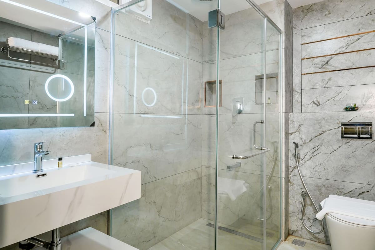 A modern bathroom with a glass-enclosed shower, a white sink, and a marble-tiled wall.