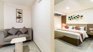 A hotel room with a sofa, a small table, a bed with a headboard, and a wall with a floral art piece. - Hotel Star Place - Chennai (Chennai)