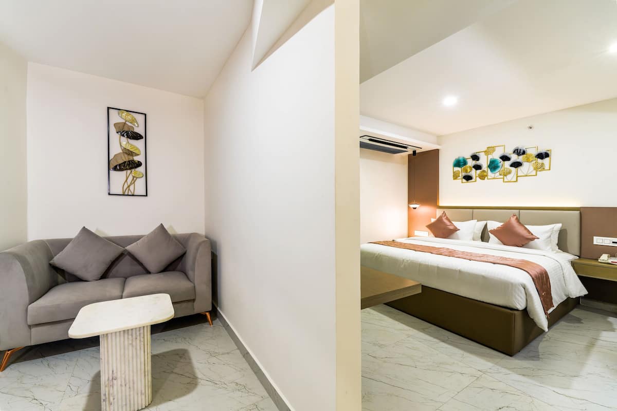 A hotel room with a sofa, a small table, a bed with a headboard, and a wall with a floral art piece.