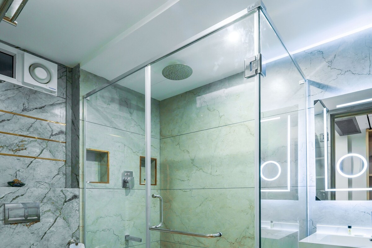 A modern bathroom with a glass-enclosed shower, marble walls, and a white sink.