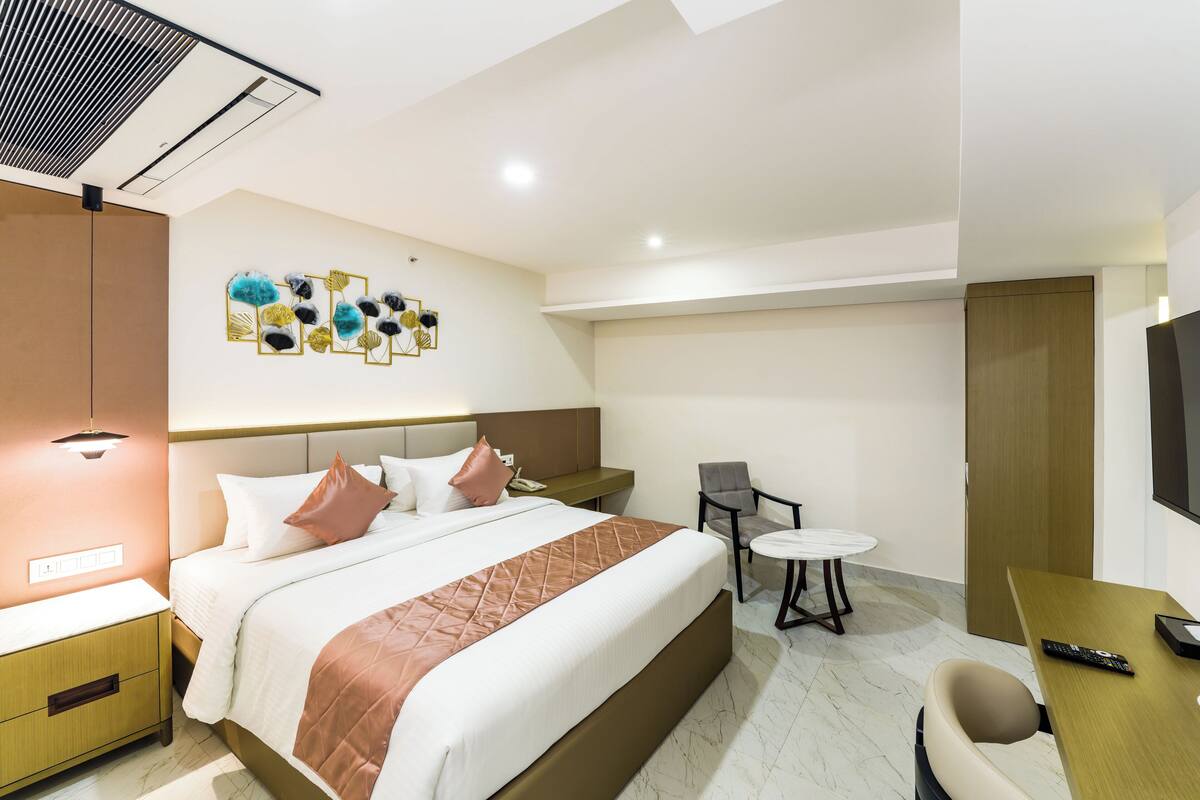 A hotel room with a bed, bedside table, chair, desk, and a flat-screen TV.