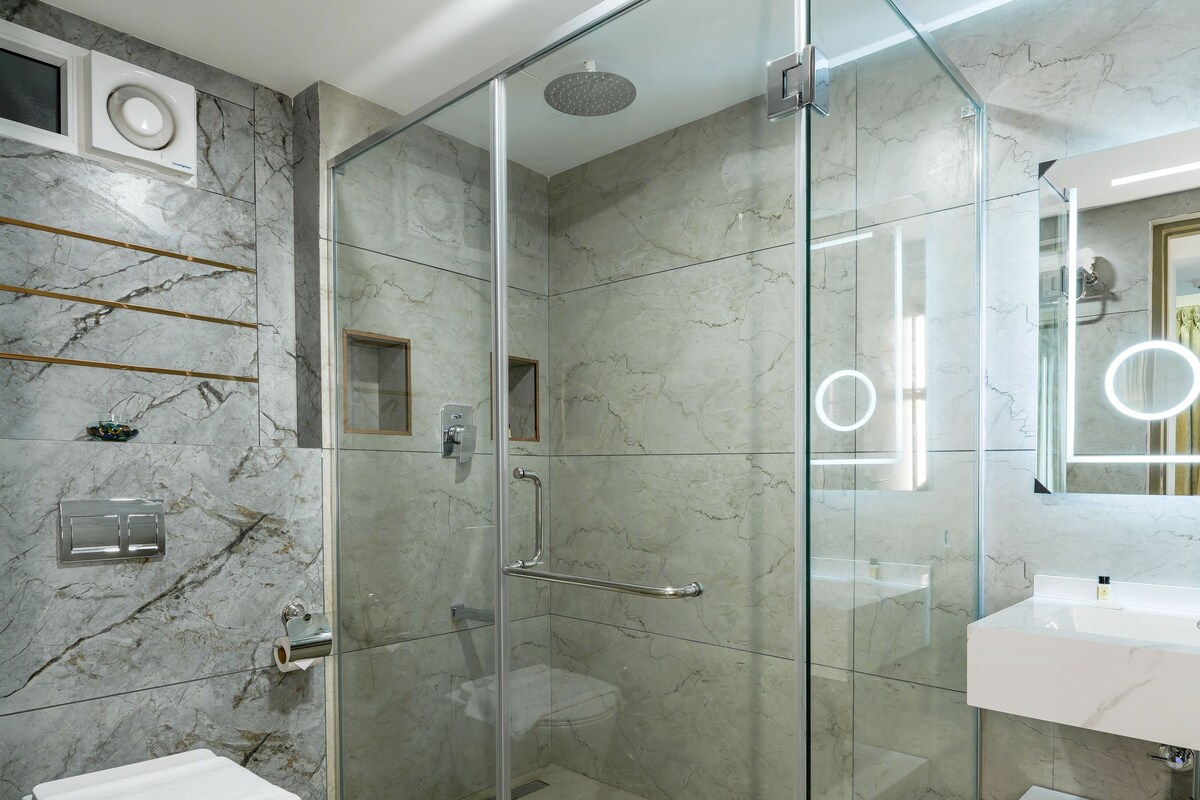 A modern bathroom with a glass-enclosed shower, a white sink, and marble walls.