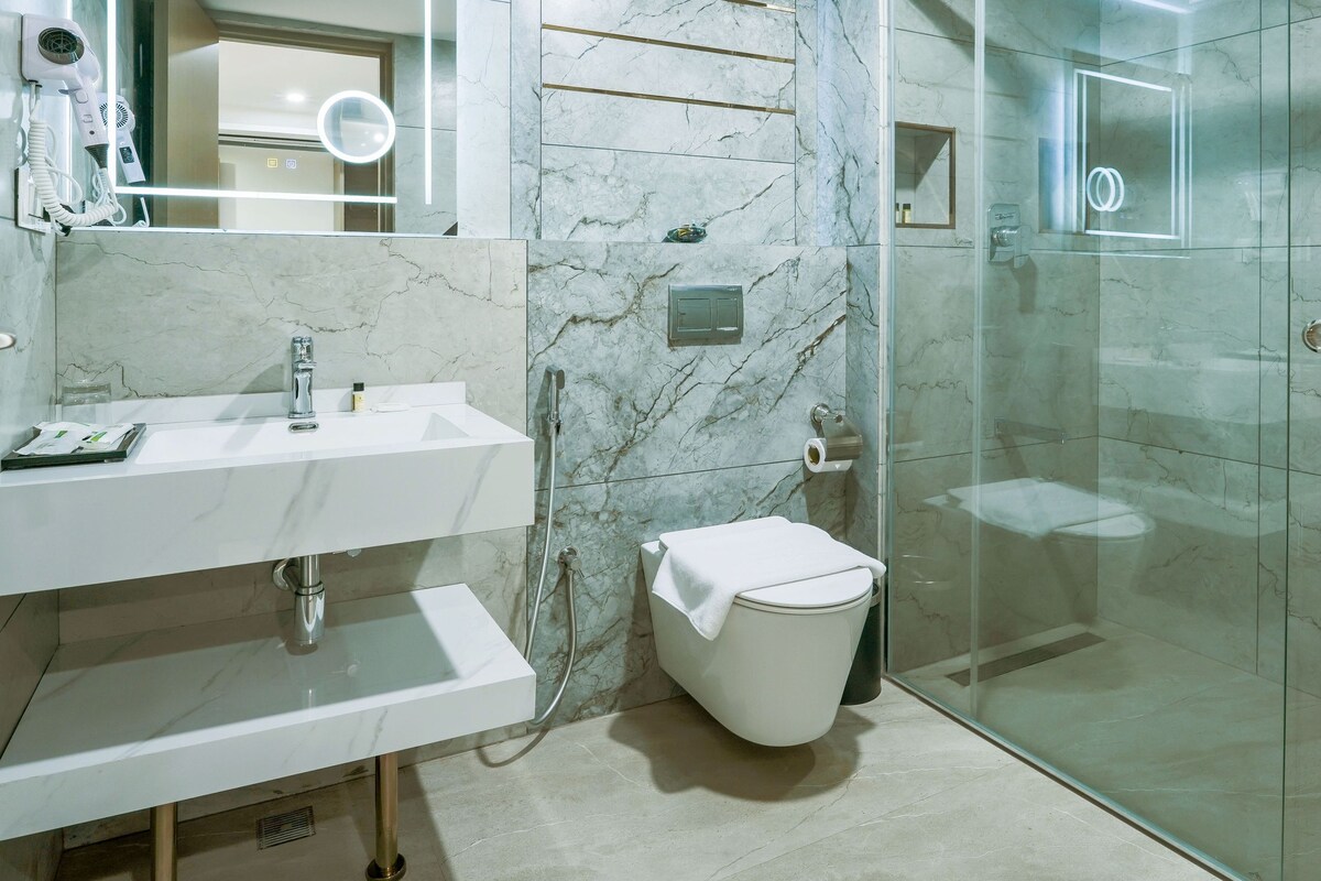 Une salle de bain moderne avec un meuble-lavabo en marbre, une douche en verre et un grand miroir doté d’un éclairage intégré.
