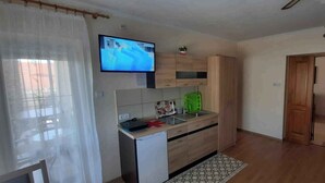 Eine kompakte Küche mit Flachbildfernseher, Holzschränken, einem kleinen Kühlschrank und einem Essbereich mit Tisch und Stühlen.