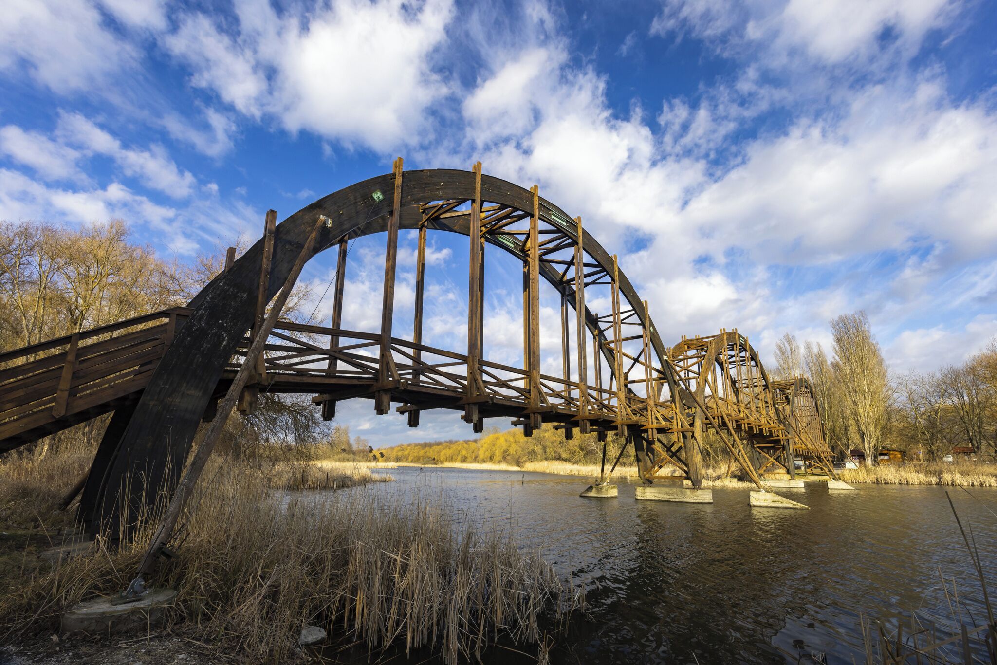 Grande struttura storica di una ruota idraulica con un ponte di legno che scavalca un fiume.