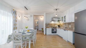 Una cuina moderna amb armaris blancs, un frigorífic d'acer inoxidable i una zona de menjador amb taula preparada per a quatre.