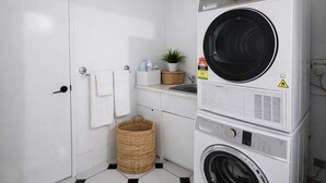 Une petite buanderie comprenant une machine à laver et un sèche-linge superposés, un petit évier, un panier en osier et une plante en pot.