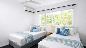Une chambre avec deux lits, un ventilateur de plafond, un appareil de climatisation et une fenêtre donnant sur un paysage verdoyant.