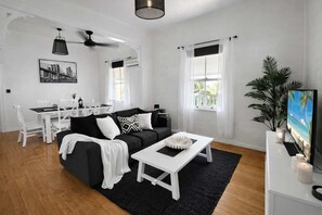 Una sala de estar moderna con un sofá negro, una mesita de centro blanca y un comedor con mobiliario blanco.