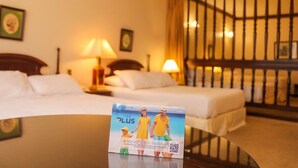 A hotel room with two beds, a nightstand, a lamp, and a view of the sea through a window with a curtain. - Family Escape in Asunción | Relaxing Stay w/ Spa, Gym & Pool Access (Asunción)