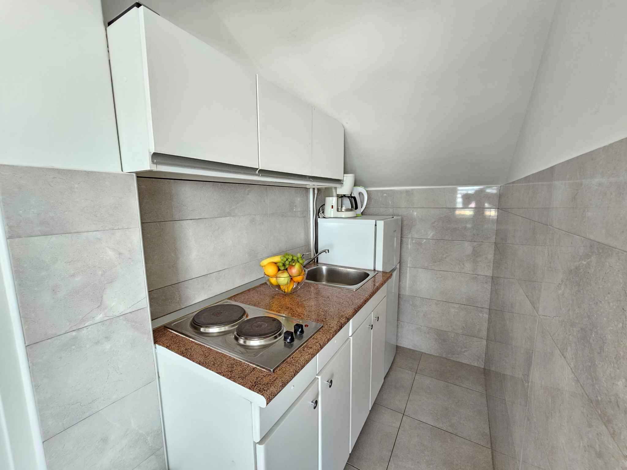Uma cozinha compacta com armários brancos, bancada de granito, fogão a gás, cafeteira e pia.