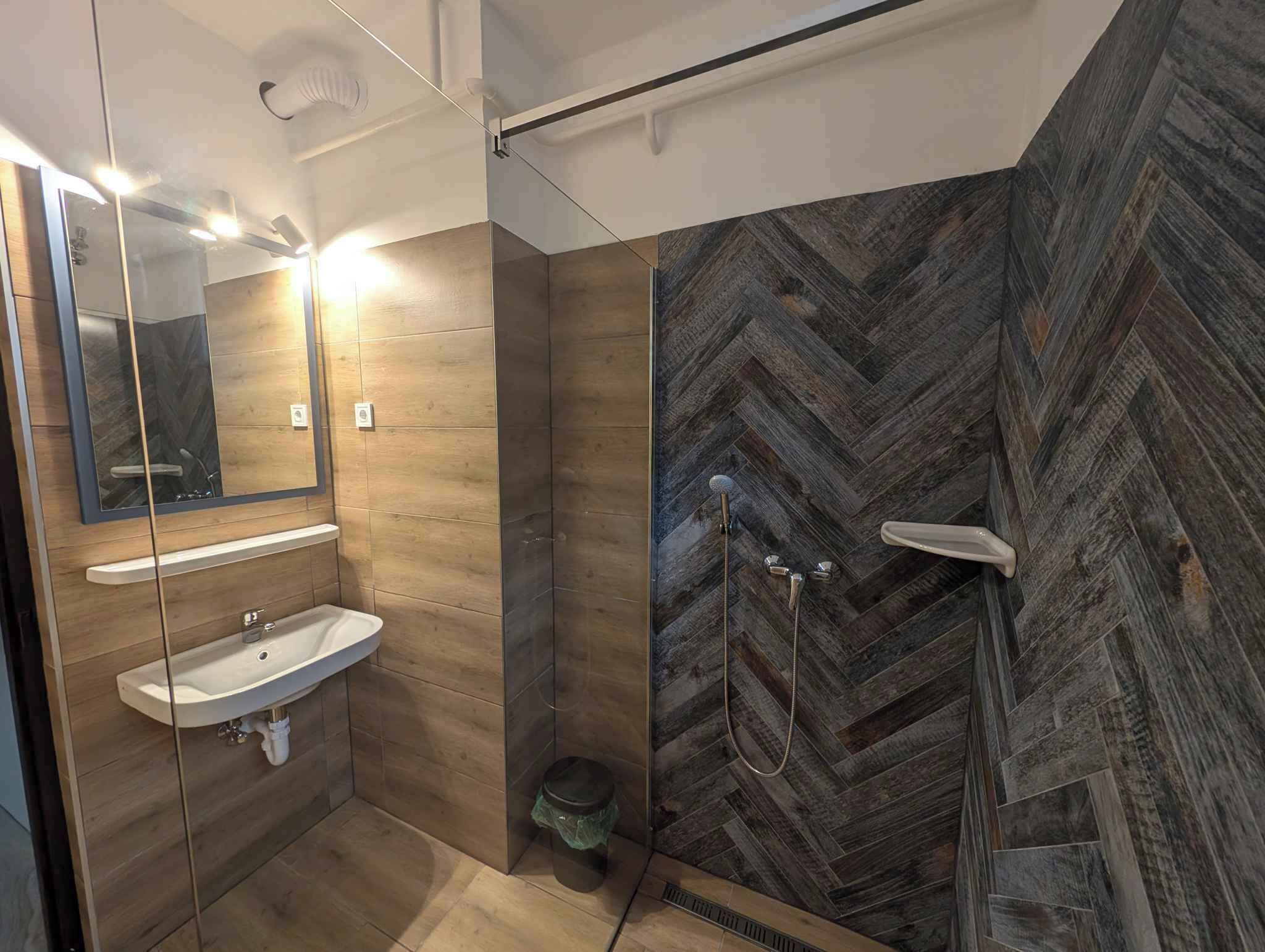 Une salle de bain moderne avec un meuble-lavabo en bois, un grand miroir et un mur de douche orné d’un motif en chevrons.
