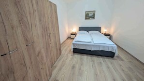 A bedroom with a wooden wardrobe, a bed with white bedding, two bedside tables with lamps, and a painting on the wall. - Holiday apartment with WLAN and air conditioning (Zamárdi)