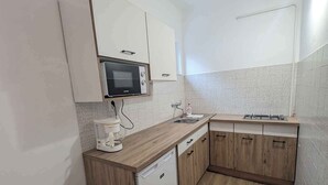 A compact kitchen with a microwave, coffee maker, sink, and wooden cabinets. - Holiday apartment with WLAN and air conditioning (Zamárdi)