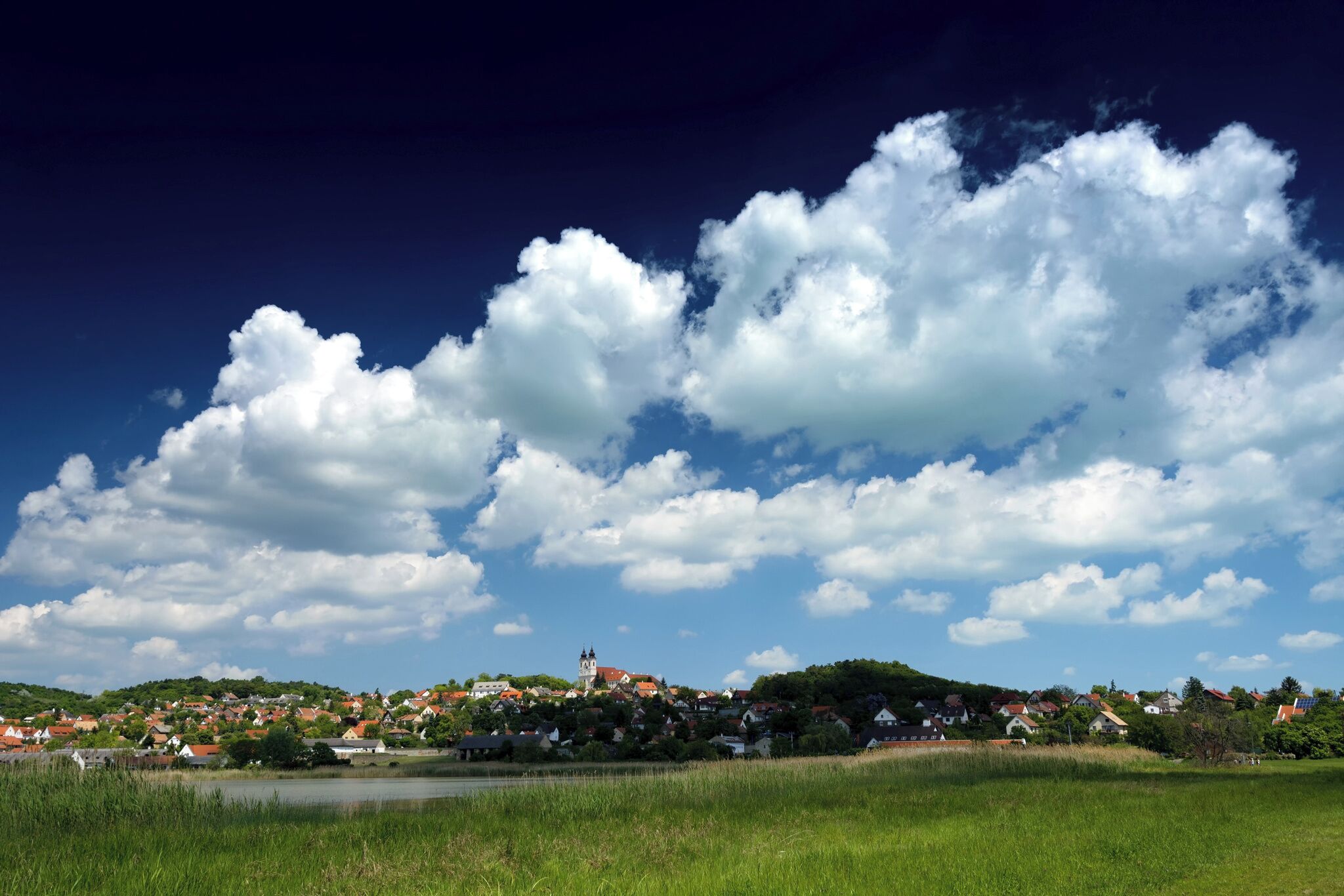 A town with a prominent church on a hill, surrounded by green fields and a body of water.