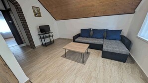 Ein Wohnzimmer mit Holzboden, einem schwarzen Sofa mit blauen Kissen, einem Couchtisch aus Holz und einem Fernseher auf einem Lowboard.