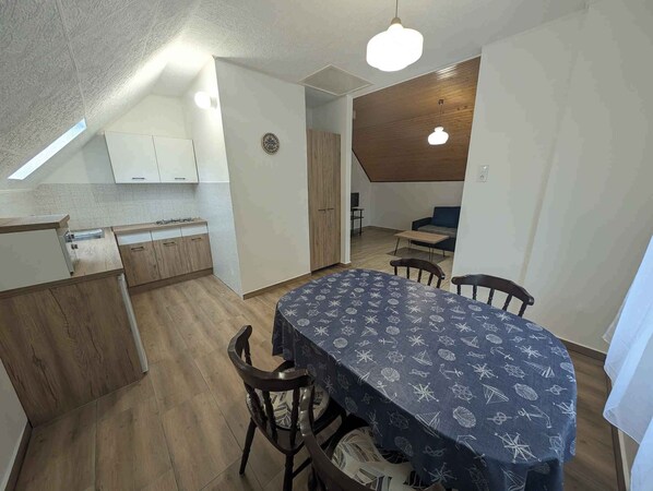 A compact kitchen with wooden cabinets and a dining area with a table covered in a patterned tablecloth. - Holiday apartment with Wi-Fi, terrace and air conditioning (Zamárdi)