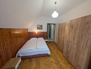 A bedroom with a wooden headboard, a bed with white linens, a wooden wardrobe, and a small bedside table. - Holiday apartment with Wi-Fi, terrace and air conditioning (Zamárdi)