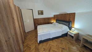 Ein Schlafzimmer mit Holzboden, einem Bett mit weißer Bettwäsche, einem Nachttisch mit Lampe und einem Holzschrank.