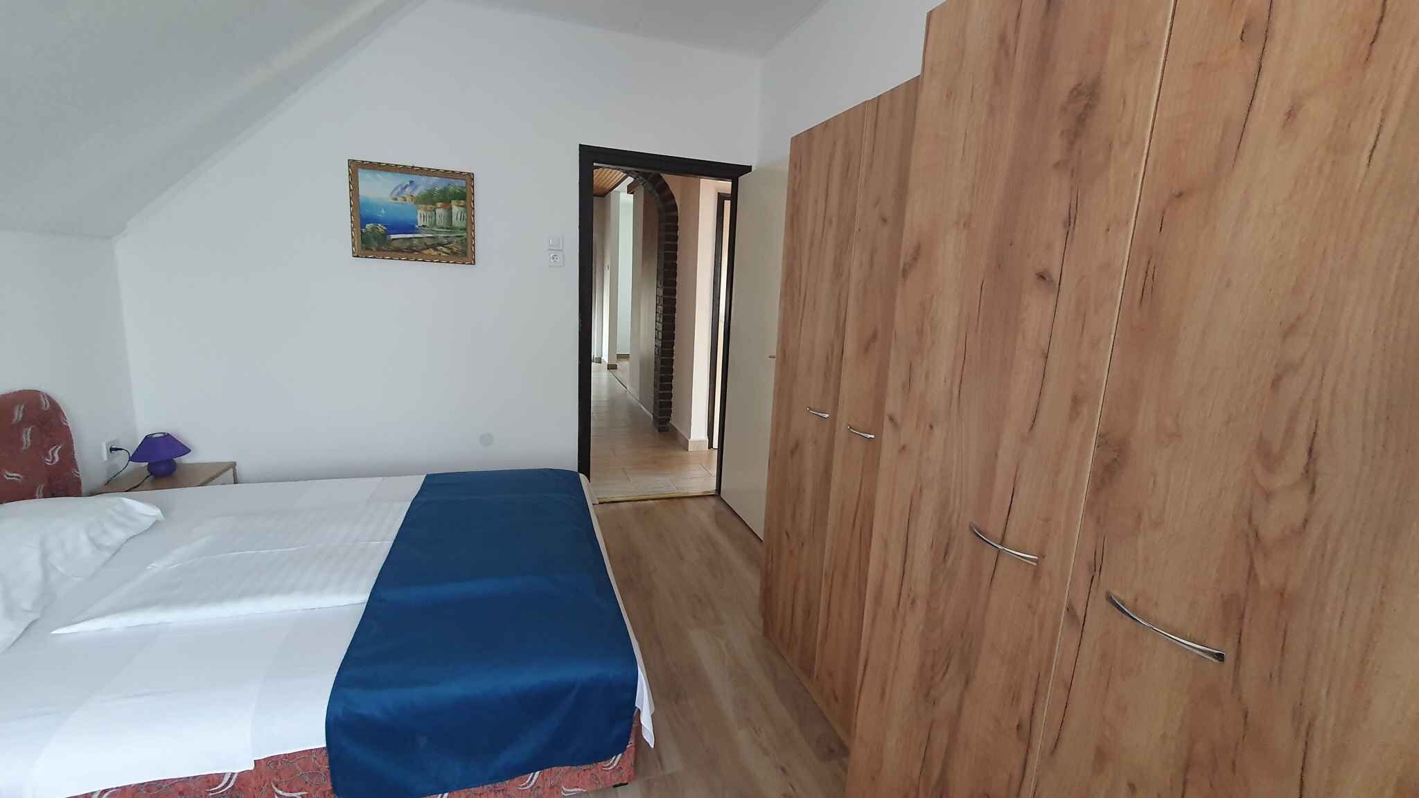 A bedroom with a bed, a wooden wardrobe, and a painting on the wall.