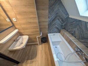 A modern bathroom with a wooden floor, a sink, a bathtub, and a herringbone-patterned wall. - Holiday apartment with Wi-Fi, terrace and air conditioning (Zamárdi)