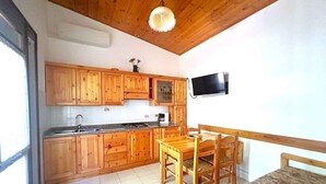 Una cucina con mobili in legno, un tavolo da pranzo con sedie, un televisore montato a parete e una finestra.