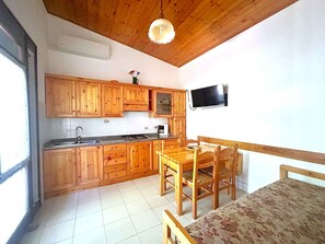 Eine Küche mit Holzausstattung, einem Esstisch mit Stühlen, einem an der Wand montierten Fernseher und einem Fenster.