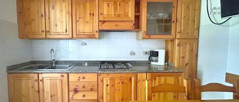 Una cocina con armarios de madera, un lavamanos, una estufa y una cafetera.