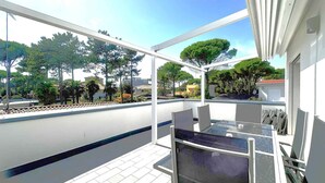 A balcony with a glass table and chairs, a tiled floor, and a view of trees and buildings. - Holiday apartment on the first floor with a large terrace (Bibione)