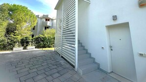 A modern building with a white exterior, a set of stairs leading to a door, and a paved driveway. - Holiday apartment on the first floor with a large terrace (Bibione)