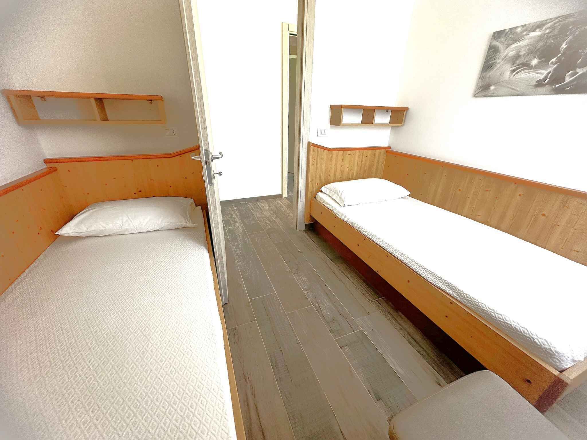 Une pièce étroite avec deux lits simples, des têtes de lit en bois, une petite étagère et une porte donnant sur une autre pièce.