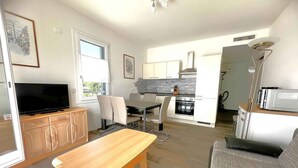 A modern living room with a TV, wooden table, and a sofa. A kitchen with a stove and microwave is visible in the background. - Holiday apartment on the first floor with a large terrace (Bibione)
