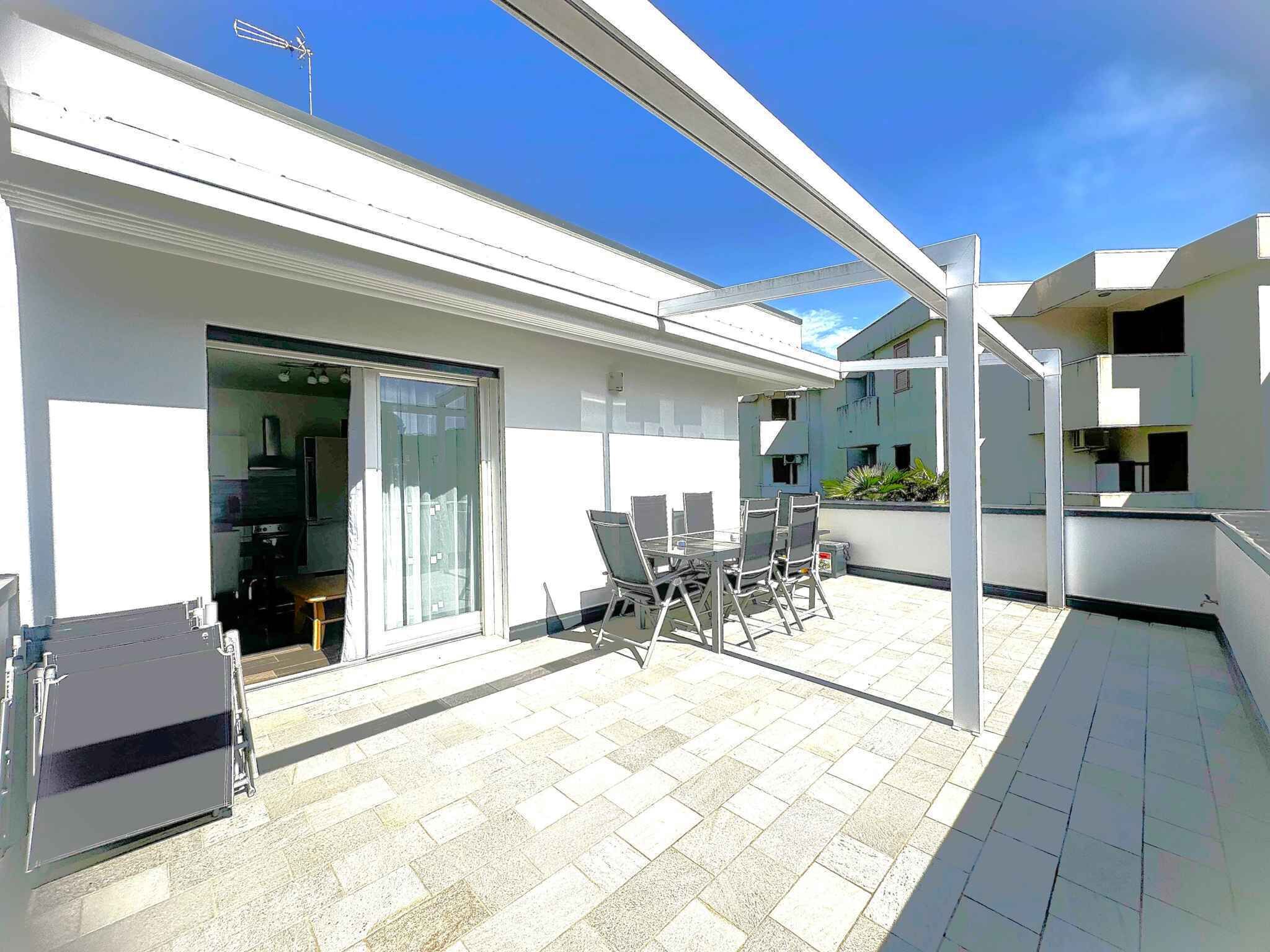 A modern outdoor patio with a glass door leading to a kitchen, a dining area with chairs, and a small table.